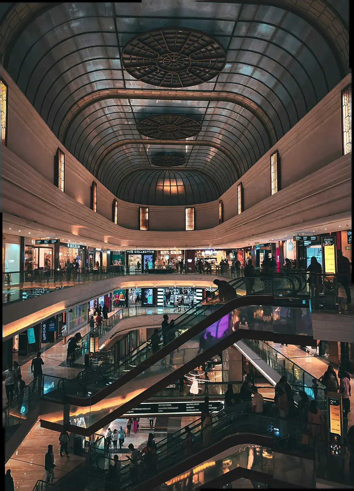 Shoppers on escalators beneath the vaulted glass ceiling of a shopping mall atrium